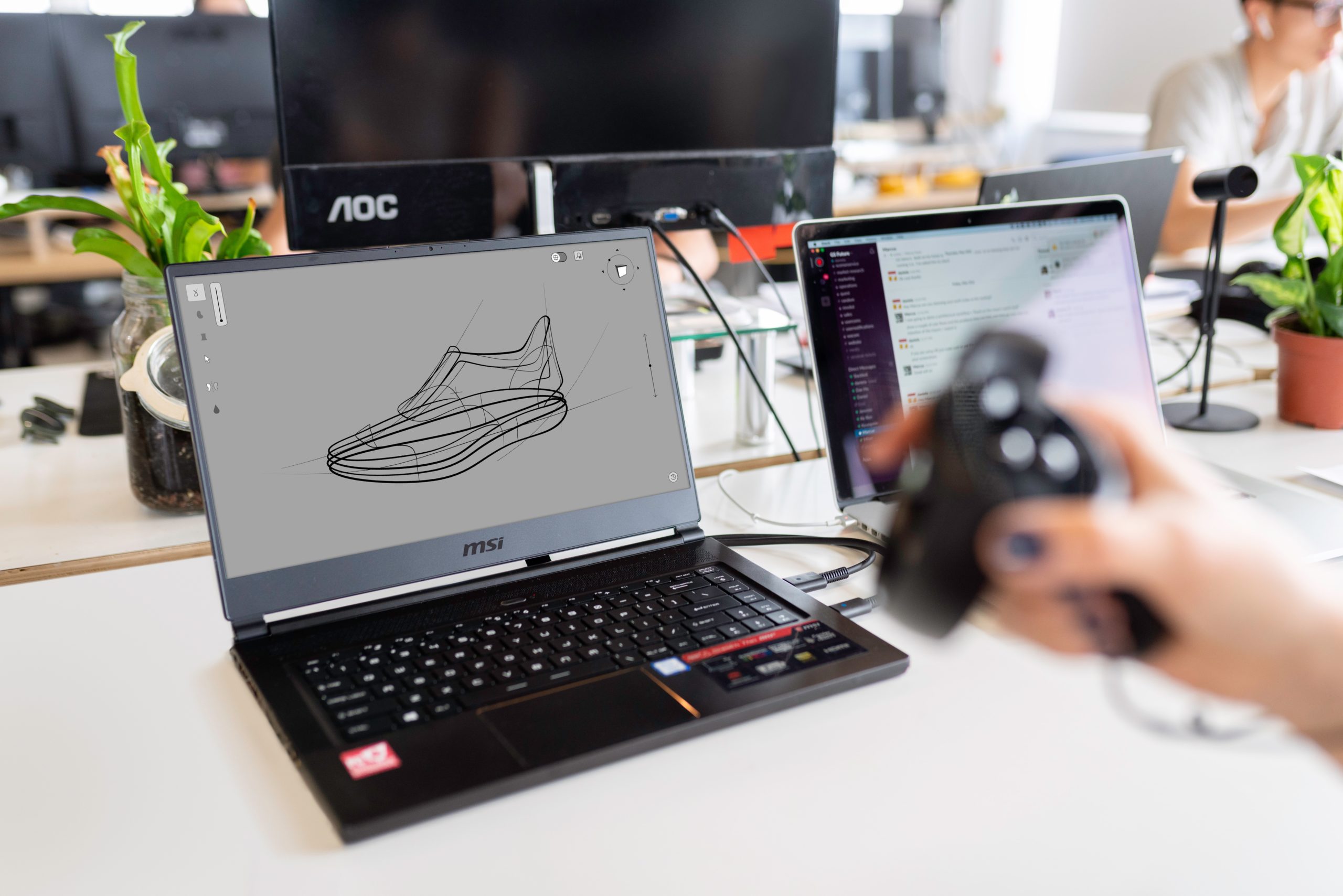 Designer using a controller beside a laptop displaying a shoe model