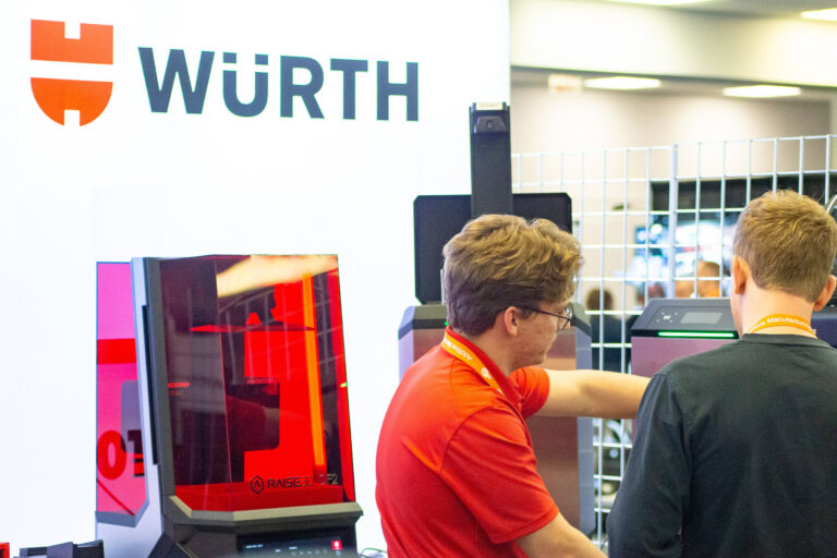 Two people beside a 3D printer at a Würth exhibition stand.