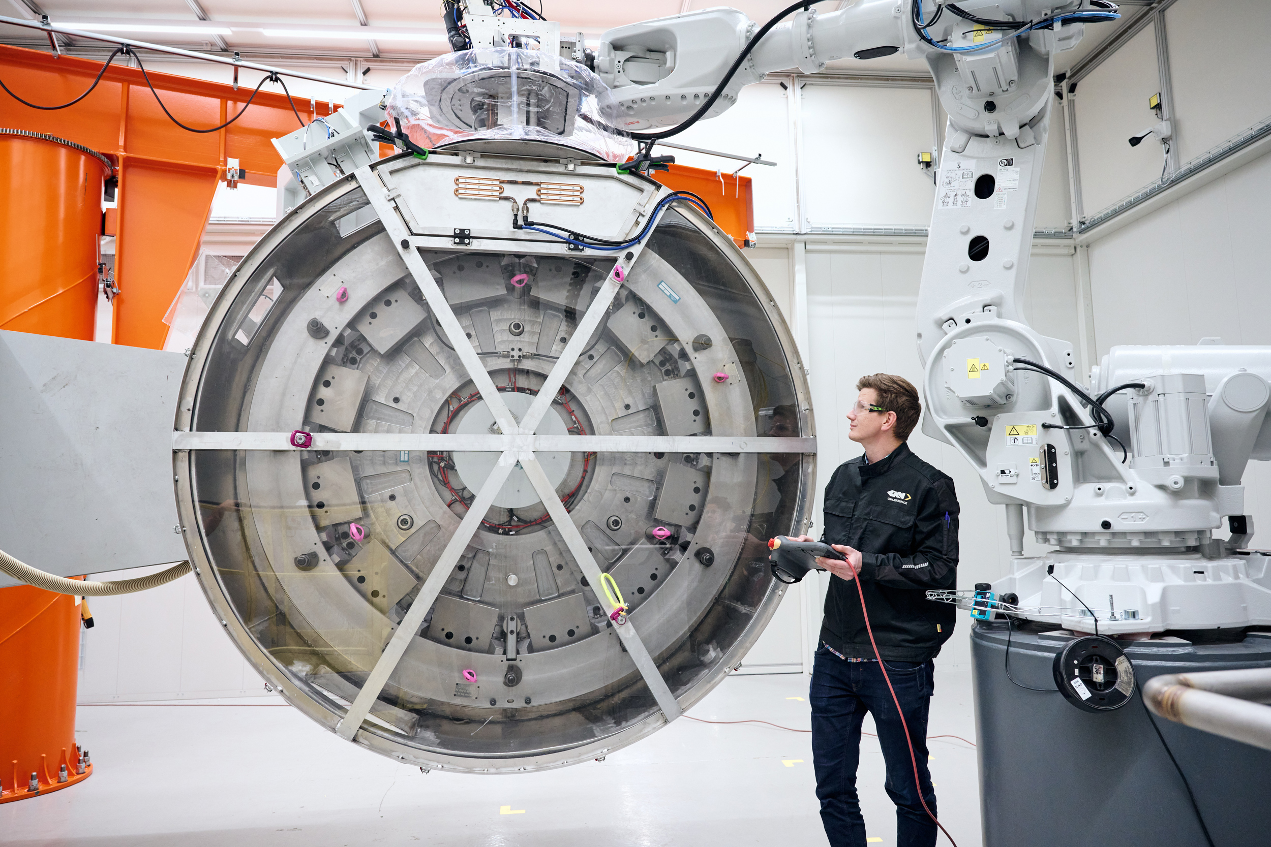 Operator beside a large circular component and an industrial robot