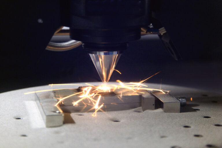 Tête laser en action sur une pièce métallique, avec des étincelles au point de travail