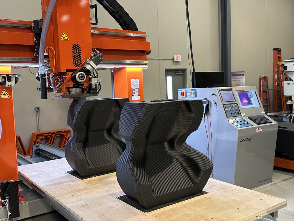 Thermwood extrusion head in front of two large printed parts and a control console