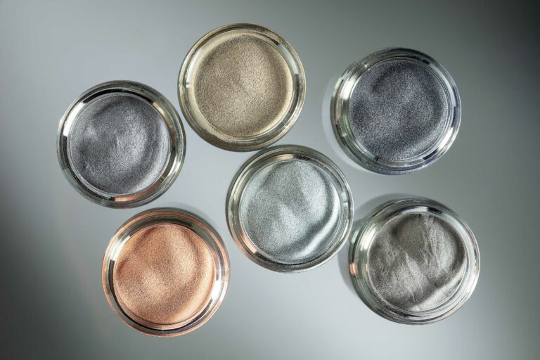 Six glass dishes containing metal powders of different colours