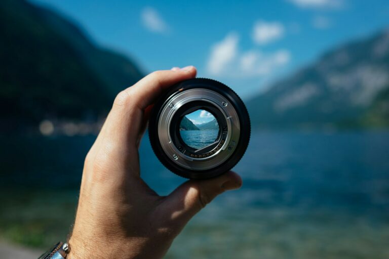 Camera lens held in front of a mountain and lake landscape