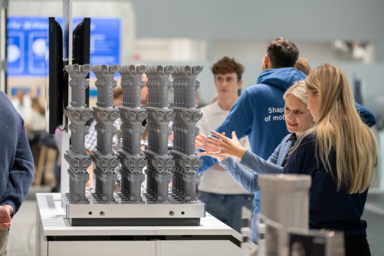 Visiteurs discutant de pièces métalliques sur un plateau de fabrication à Formnext.