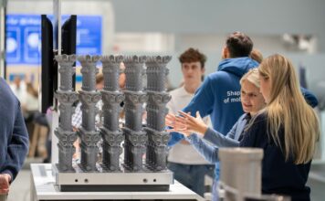 Two women discussing in front of a build platform of 3D printed parts