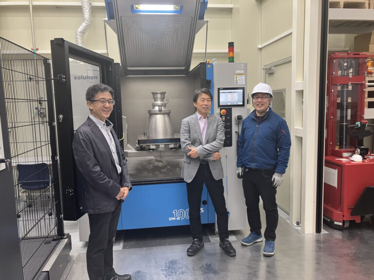 Three people beside a Solukon depowdering system at Nikon.
