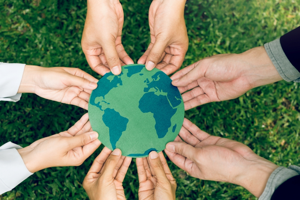 6 hands holding a map of the world painted in green