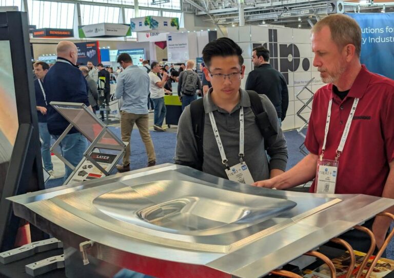 One expert showing a booth visitor a Cut Layer part on display at RAPID+TCT 2026