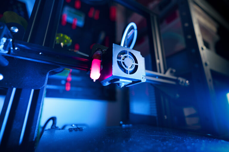 Industrial additive manufacturing equipment illuminated in blue.