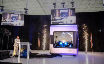 AMPERA Founder and CEO Brian Matthews pulls curtain revealing the first full-scale 3D printed reactor module, featuring a fully 3D printed silicon carbide reactor core and reactor pressure vessel at a celebratory event at the company’s innovation center in Palm Beach Gardens, Fla. (PRNewsfoto/AMPERA)