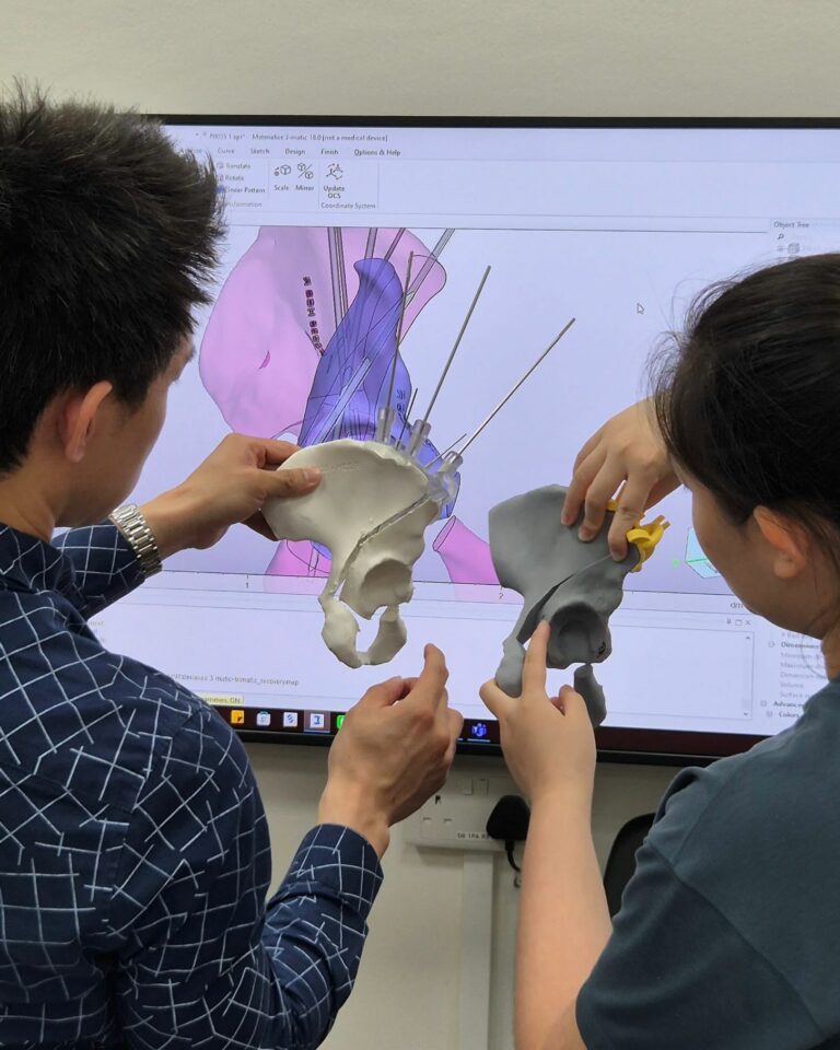 Two healthcare professionals examining an anatomical model beside a computer.