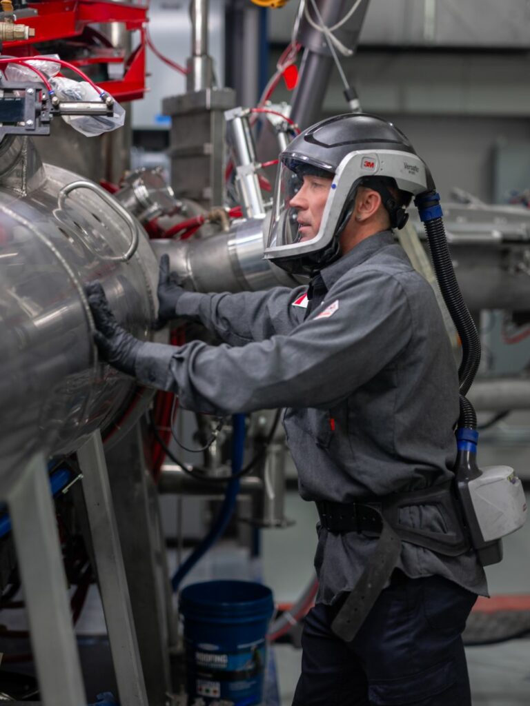 Operator in protective clothing beside industrial equipment.