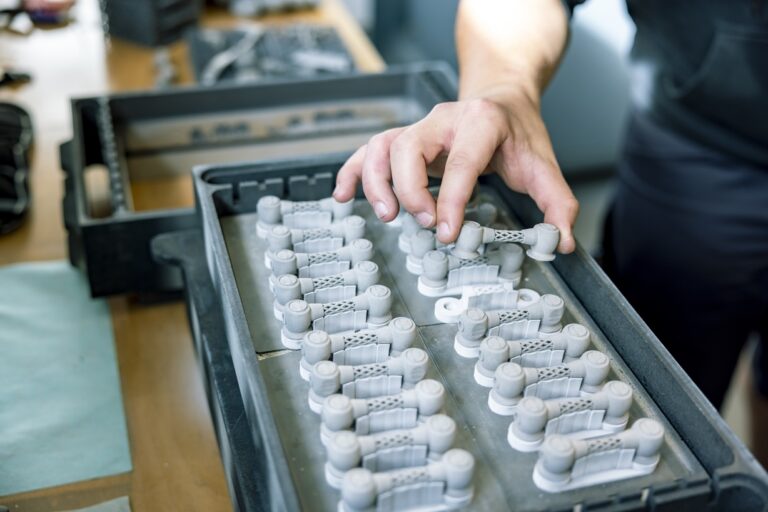 Hands holding a tray of white printed components.