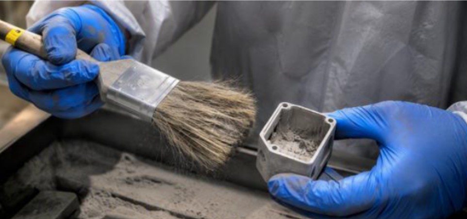 Gloved hands brushing loose powder from a metal component at Dou Yee Technologies.