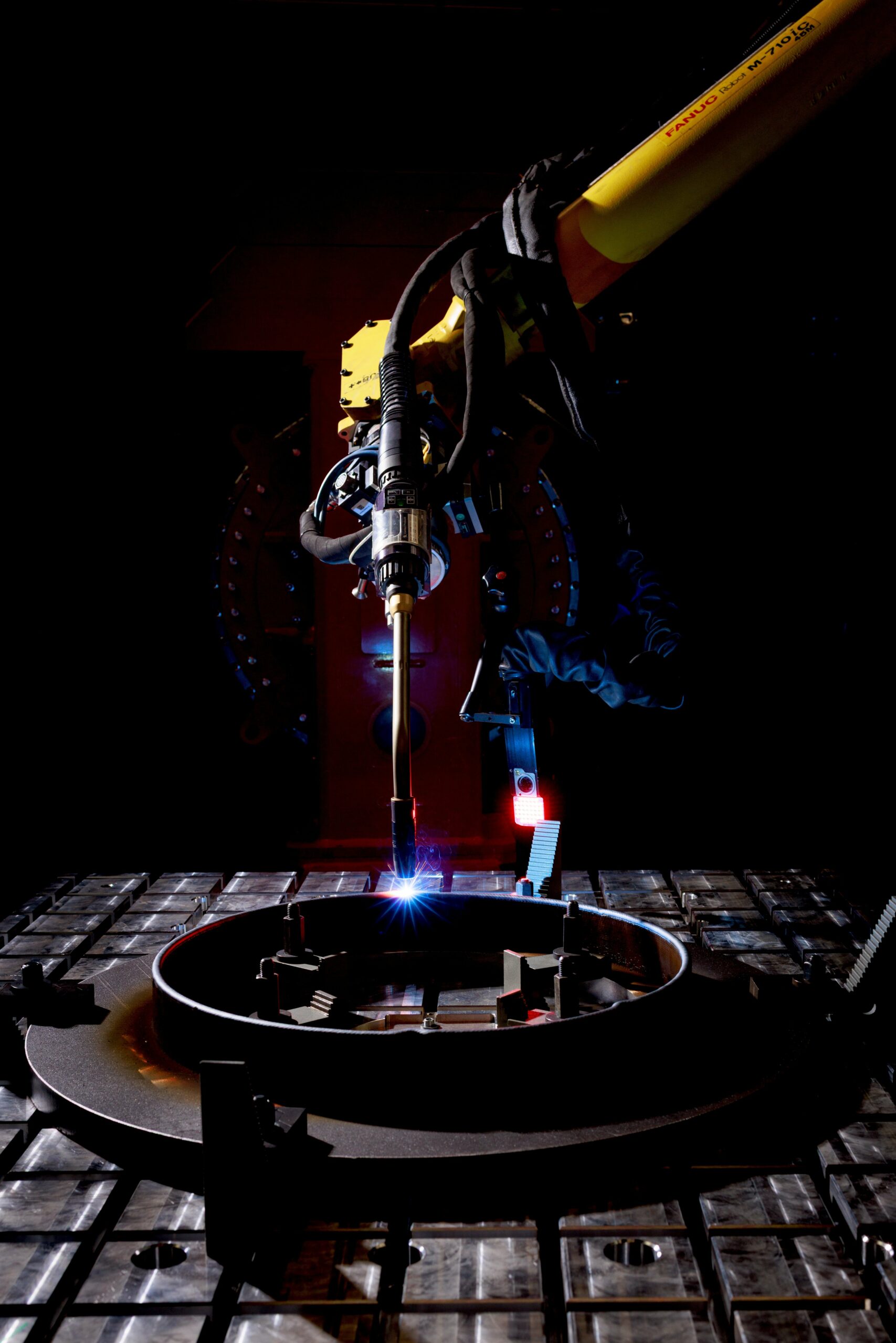 Robotic welding torch depositing metal on a circular workpiece.